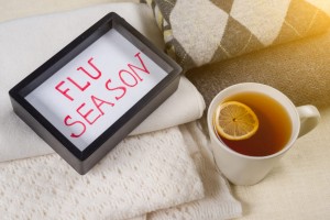 Flu season text in frame. Background warm woolen clothes, cup of hot tea.